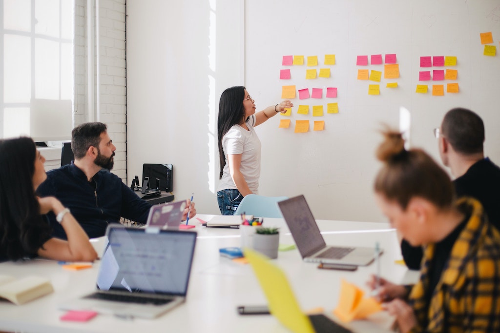 Group of people having a meeting, sticky notes on the wall outlining a plan.