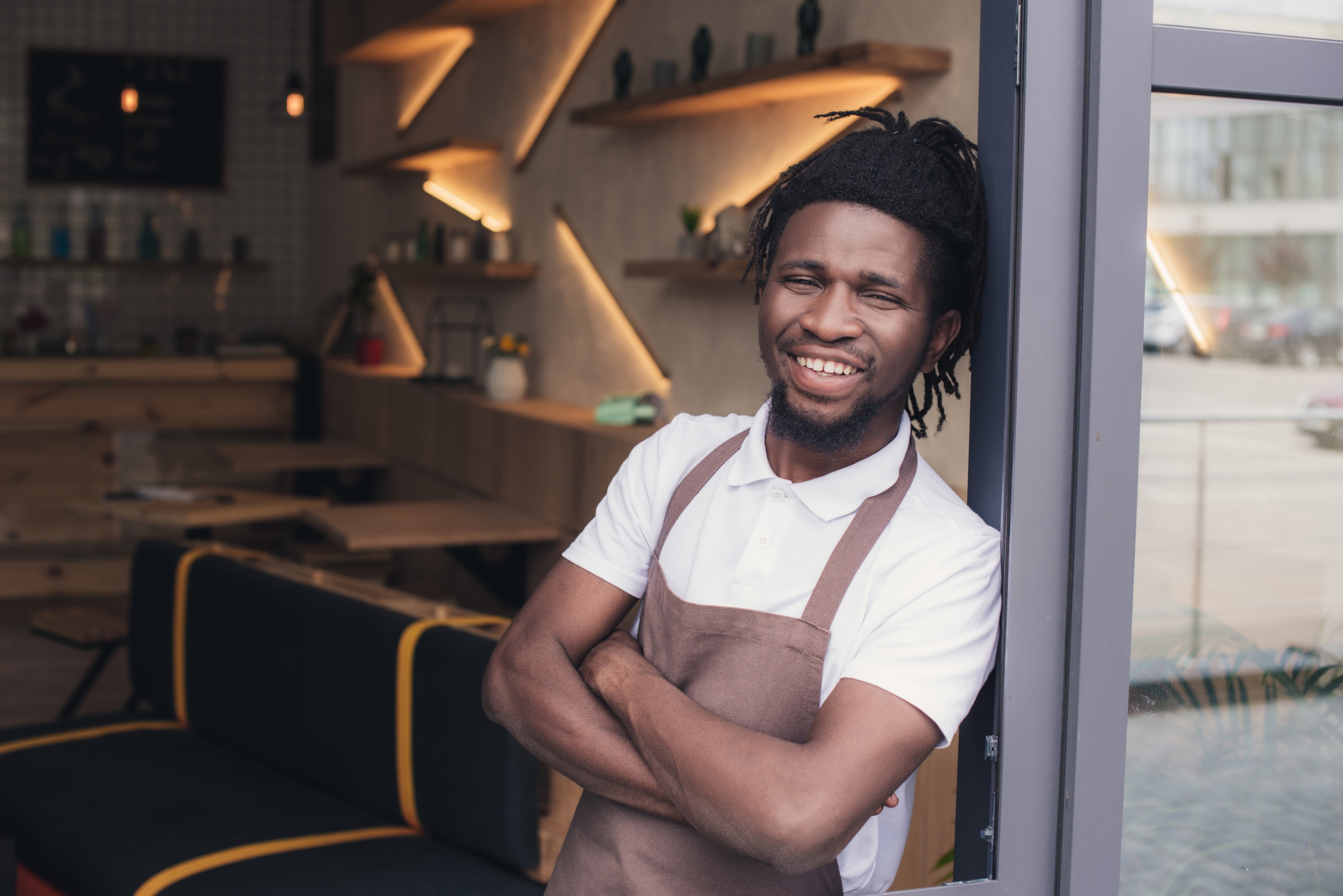 cheerful african american cafe owner in apron standing at entrance