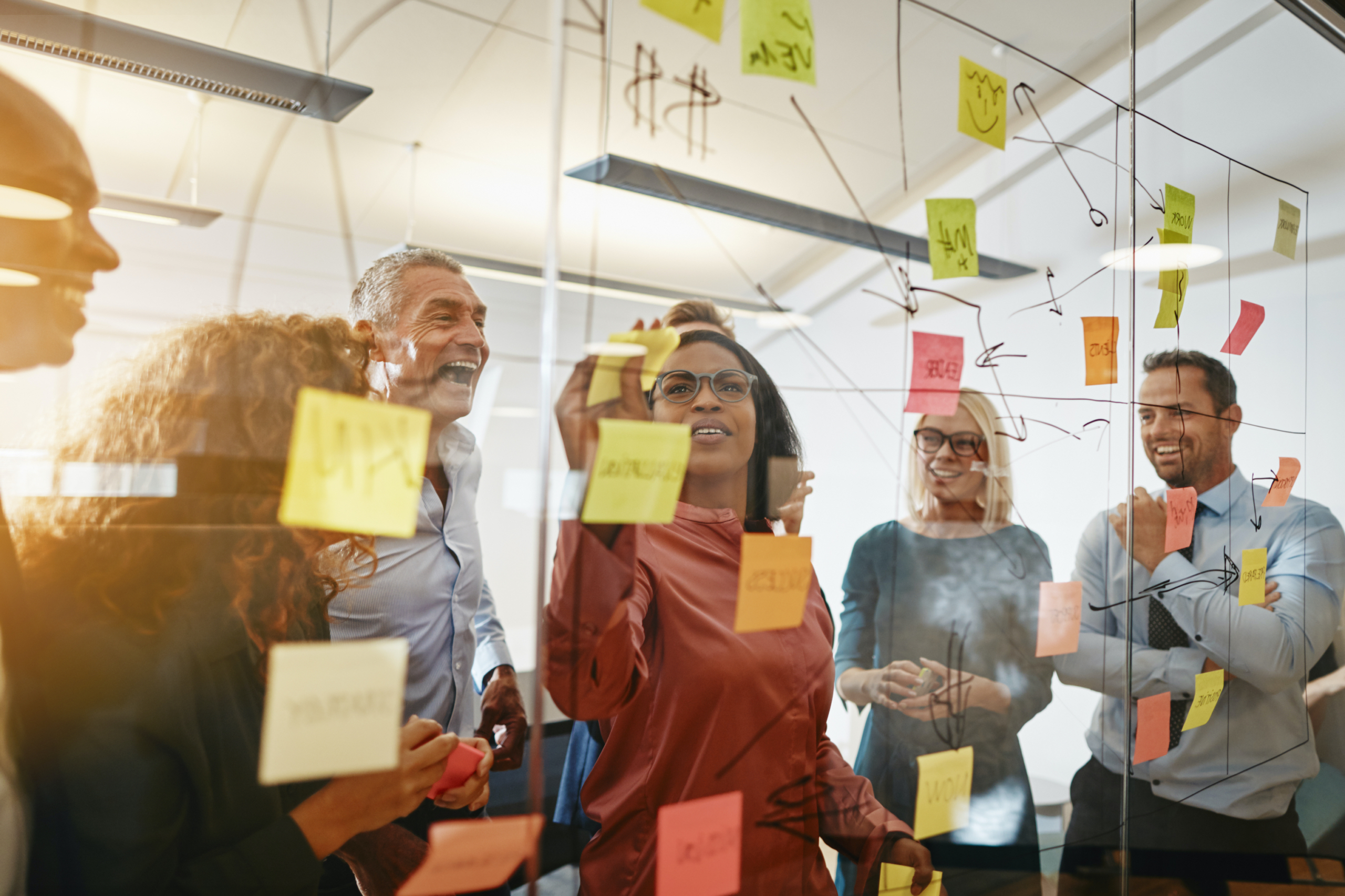 Young African businesswoman and her diverse team brainstorming with sticky notes on a glass wall while working together in a modern office.