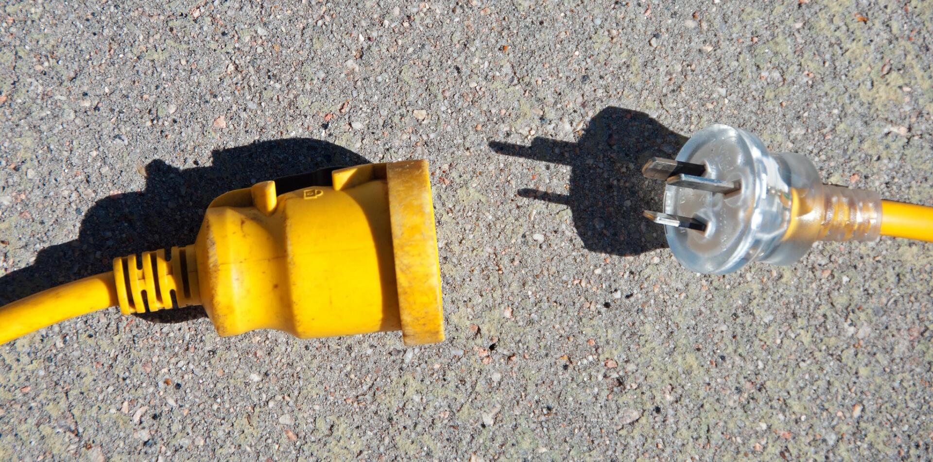 Image of a yellow plug disconnected from a yellow socket lying on asphalt