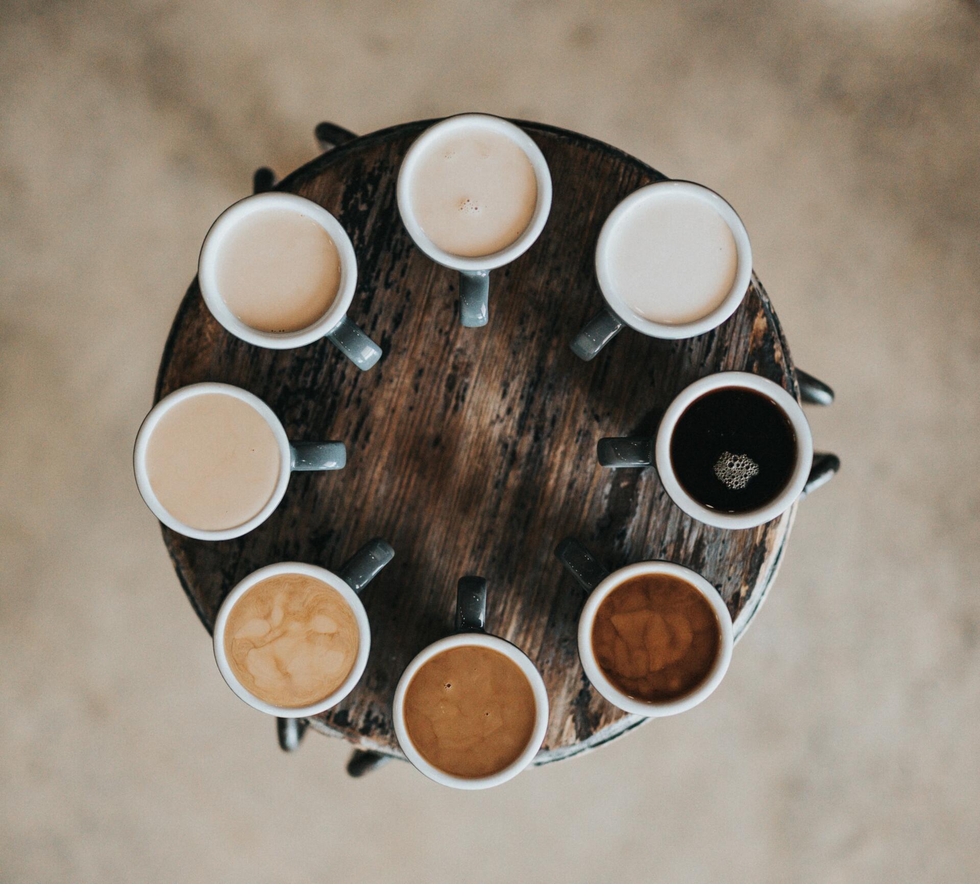 Several cups of coffee in varying shades meant to represent diversity displayed in a circle on a small table, viewed from above.